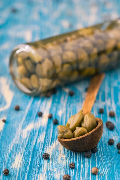 Paar kappertjes in houten lepel om expressies te jar op blauwe bord — Stockfoto