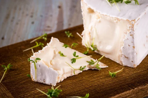 Unusual Camembert cheese with cube shape with spilled green cress on wooden board — Stock Photo, Image