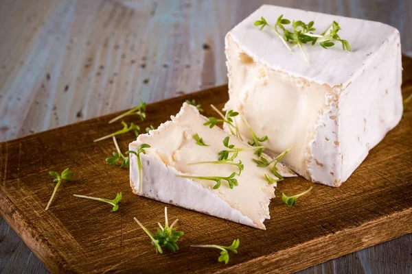 Unusual Camembert cheese with cube shape and spilled green cress on wooden board — Stock Photo, Image