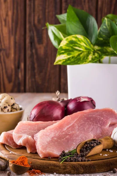 Три ломтика сырой свинины на деревянной тарелке со специями — стоковое фото