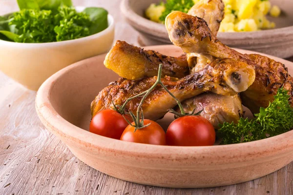 Куриные окорочка на тарелке перед картофелем и зеленым салатом — стоковое фото