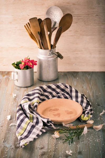 Empty clay plate on wooden board with kitchen utensils around — Stock Photo, Image
