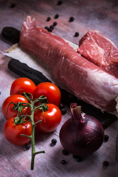 木の板に豚ヒレ肉の横にあるいくつかの赤チェリー トマト — ストック写真