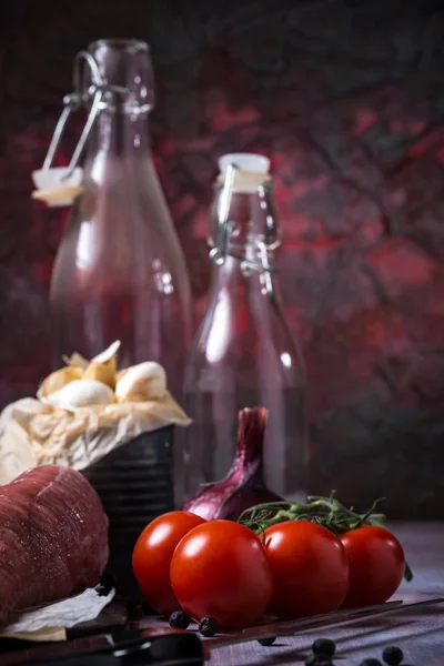 Red tomatoes next to whole pork tenderloin meat on vintage board and garlic — Stock Photo, Image