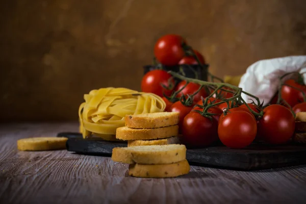 Pomodori rossi ciliegia su tavolo vintage in legno con tagliatelle e bruschette — Foto Stock