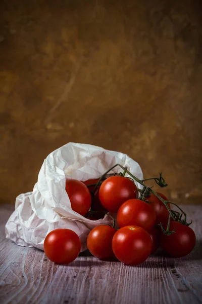 Varios tomates cherry en rama verde en bolsa de papel blanco —  Fotos de Stock