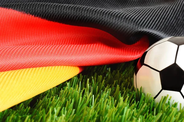 Football fan scarf in red black gold colors as national Germany flag with ball on green field grass