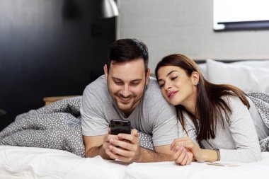 Couple in bed with electronic devices in morning