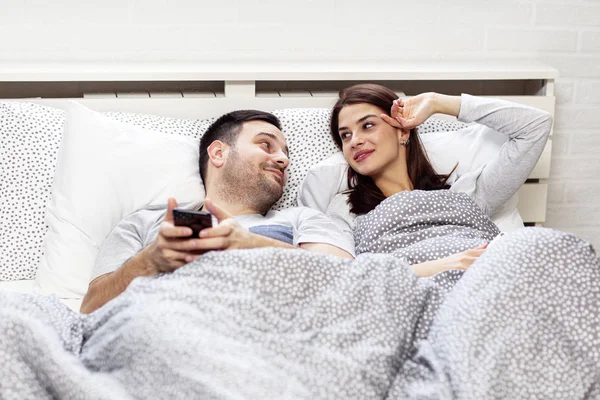 Couple in bed with electronic devices in morning