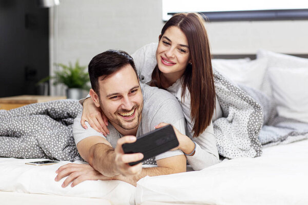 Young couple lying in bed and taking selfie by mobile phone