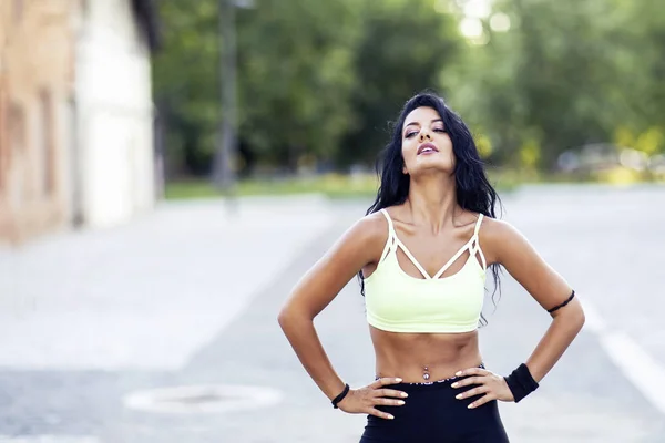 Spor kıyafetli, uzun saçlı bir kadın sokakta dikiliyor.