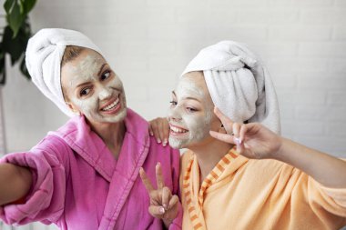 Anne ve kızı telefonda yüzlerinde maske ve kafalarında havluyla selfie çekiyorlar.