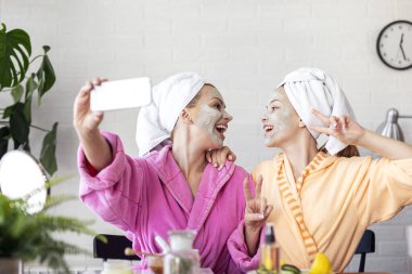 Anne ve kızı telefonda yüzlerinde maske ve kafalarında havluyla selfie çekiyorlar.