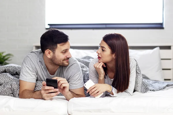 Sabah yatağında cep telefonu olan bir çift.