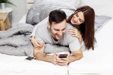 Young couple lyuing in bed with mobile phone on hand