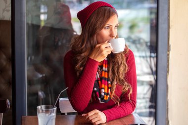 Beautiful girl in red drinking coffe in local cafe and glass of lemonade with straw on table