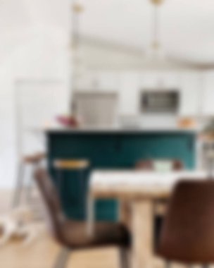 Ada, granit tezgah, paslanmaz çelik buzdolabı, fırın ve ahşap zemini olan çağdaş beyaz bir mutfağın içi.