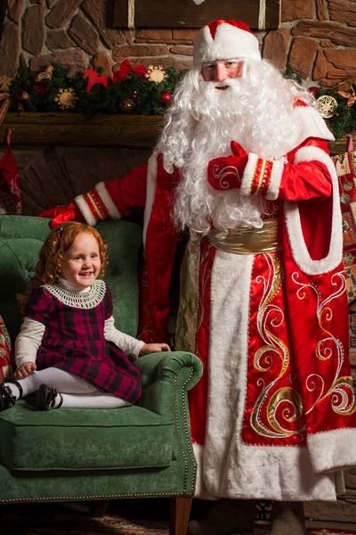 Дід Мороз дивиться на маленька дівчинка, що сидить у кріслі — стокове фото