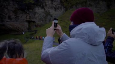REYKJAVIK, ICELAND, 10 EKİM 2019 Bir adam cep telefonuyla Seljalandsfoss şelalesinin fotoğraflarını çekiyor