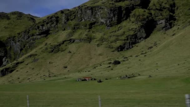 Utsikt över gröna ängar och ett ensamt hus från bilfönstret. Kullar och berg på Island — Stockvideo