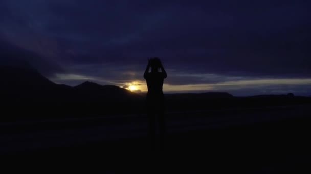 Sylwetka dziewczyny, która fotografuje zachód słońca w górach. Słońce zachodzi nad górami. — Wideo stockowe