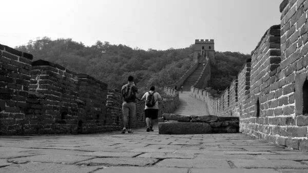 Dos turistas caminando a través de la gran muralla. Sección Mutianyu, Beijing, China. Vista desde el suelo. Fotografía en blanco y negro — Foto de Stock