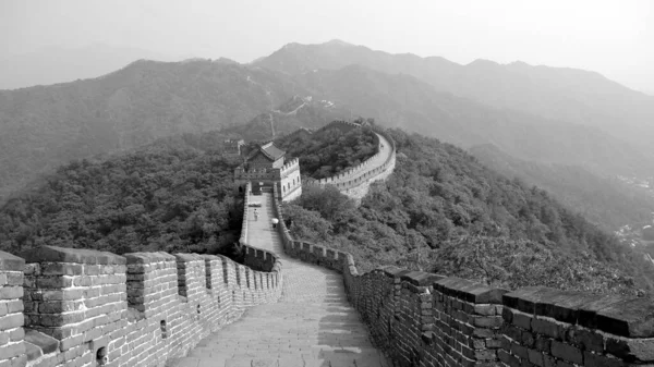 Dağ boyunca zikzak çizen ve birkaç muhafız direğini geçen büyük duvarın yolu. Yolun ortasından görüntüle. Mutianyu bölümü, Pekin, Çin. Siyah beyaz fotoğraf — Stok fotoğraf