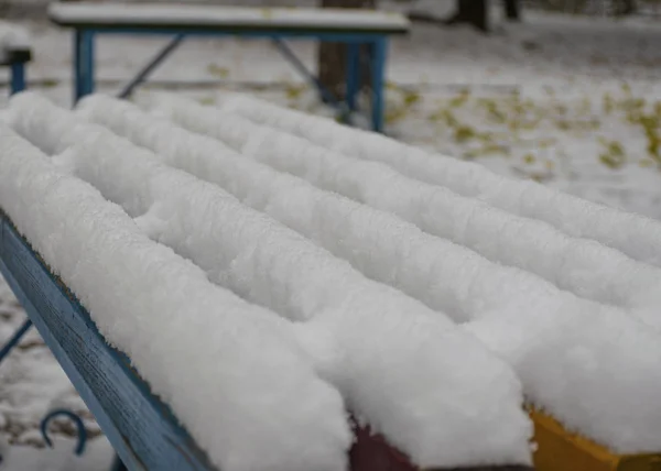 Panchina del parco coperta di neve. La prima neve della città. Tempo nevoso nuvoloso . — Foto Stock