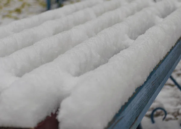 Скамейка в парке покрыта снегом. Первый снег в городе. Облачно-снежная погода . — стоковое фото
