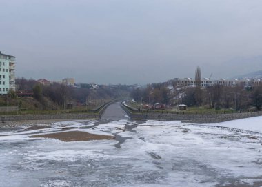 Bulutlu bir havada şehirde donmuş bir nehir. Kış geldi. Şehir manzarası.