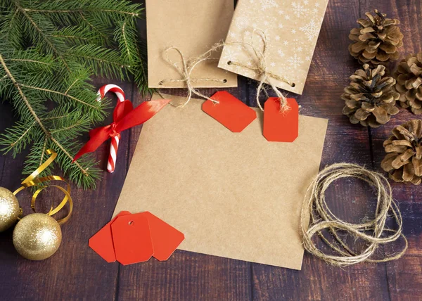 Gift bag made of handmade kraft paper on a wooden background in a Christmas style, decorated with Christmas tree balls, cones, a ball of rope, fir branches. Christmas, New Year, winter holiday.