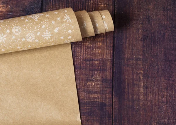 Roll of brown kraft paper with a pattern of snowflakes on a wooden background. Eco paper. Secondary, environmentally friendly. Material for package packaging. Gift wrapping paper.