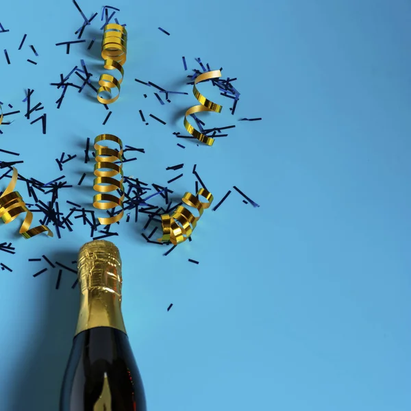 Garrafa de champanhe com confete multicolorido sobre fundo azul. Celebração — Fotografia de Stock