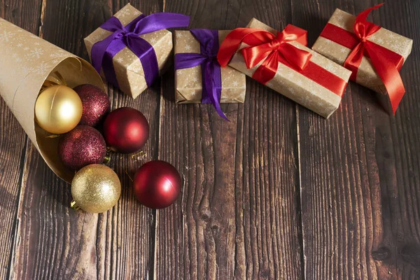 Christmas gifts, gold, silver, red Christmas balls spilled out from a package of kraft paper on a wooden background. Christmas balls. Copyspace