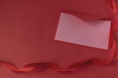 Kırmızı arka planda saten kurdeleli kırmızı bir zarf. Sevgililer Günü için sevgililer günü. Aşk