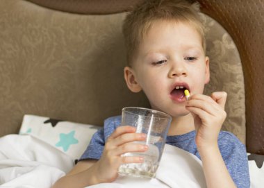 Ateşi ve baş ağrısı olan hasta üzgün bir çocuk ilaç ve hapların yanında yatıyor. Grip salgını virüsü bakterisi