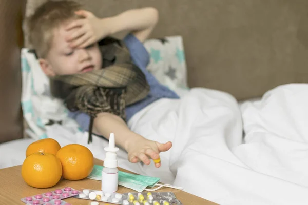 A sick sad child with a temperature and a headache lies in bed next to medication. Flu colds disease virus bacterium