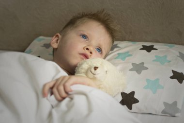 Sıcaklıktaki hasta çocuk oyuncak bir ayıyla yatakta yatıyor. Grip salgını virüsü bakterisi