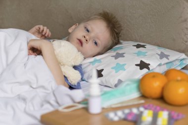 Ateşi ve baş ağrısı olan hasta üzgün bir çocuk yatakta ilacın yanında yatıyor. Grip salgını virüsü bakterisi