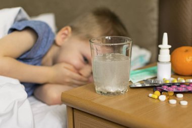 Ateşi ve baş ağrısı olan hasta üzgün bir çocuk ilaç ve hapların yanında yatıyor. Grip salgını virüsü bakterisi