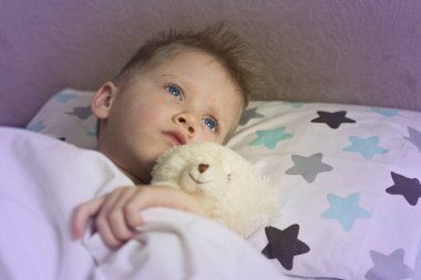 Sıcaklıktaki hasta çocuk oyuncak bir ayıyla yatakta yatıyor. Grip salgını virüsü bakterisi