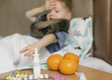 Ateşi ve baş ağrısı olan hasta üzgün bir çocuk yatakta ilacın yanında yatıyor. Grip salgını virüsü bakterisi