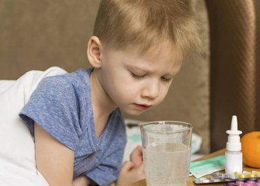 Ateşi ve baş ağrısı olan hasta üzgün bir çocuk ilaç ve hapların yanında yatıyor. Grip salgını virüsü bakterisi