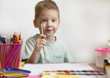Çocuk bir fırçayla resim yapar ve kağıda resim yapar. Çizim için suluboya. Okuldaki erkek sanatçı. Yaratıcılık ve hobiler