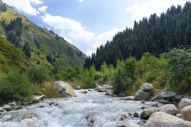 Mavi suyu olan bir dağ nehri, büyük taşlar resimli dağların arasında akar. Dağların yamaçlarının arasında mavi gökyüzü.