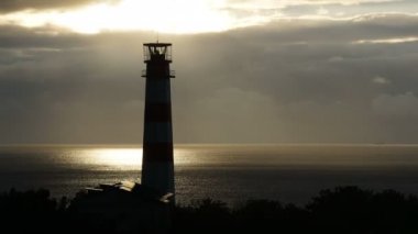 Deniz altında fırtınalı bulutlar ve arka planda gemiyle deniz feneri