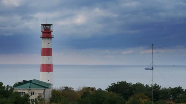 Buque de carga pasa por un hermoso faro majestuoso bajo nubes tormentosas dramáticas — Vídeo de stock