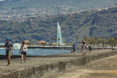 Puerto de La Cruz, Tenerife, İspanya, 12 Nisan 2017: İnsanlar eski ticari liman ve tarihi merkez yakınlarında beton bir dalgakıran boyunca yürüyorlar. Arkadaki ana Lago Martianes çeşmesi.