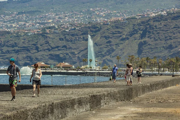 Puerto de La Cruz, Tenerife, España, 12 de abril de 2017: La gente camina a lo largo de un rompeolas de hormigón cerca del antiguo puerto comercial y el centro histórico. La fuente principal del Lago Martianes en el fondo — Foto de Stock