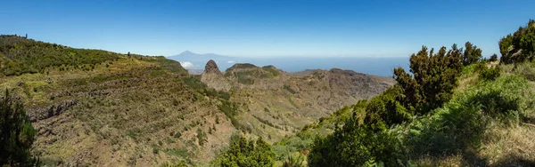 Ufuk üzerinde volkan Teide ve La Gomera Garajonay milli parkı yakınında Los Roques zirveleri ile Tenerife Adası Panoramik görünümü. Dik yeşil yamaçlarda kalıntı defne ve fundalık çalılıkları. Kanarya — Stok fotoğraf
